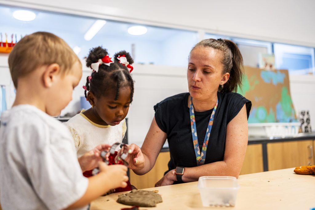 A teacher sat with two children at a table working on an activity