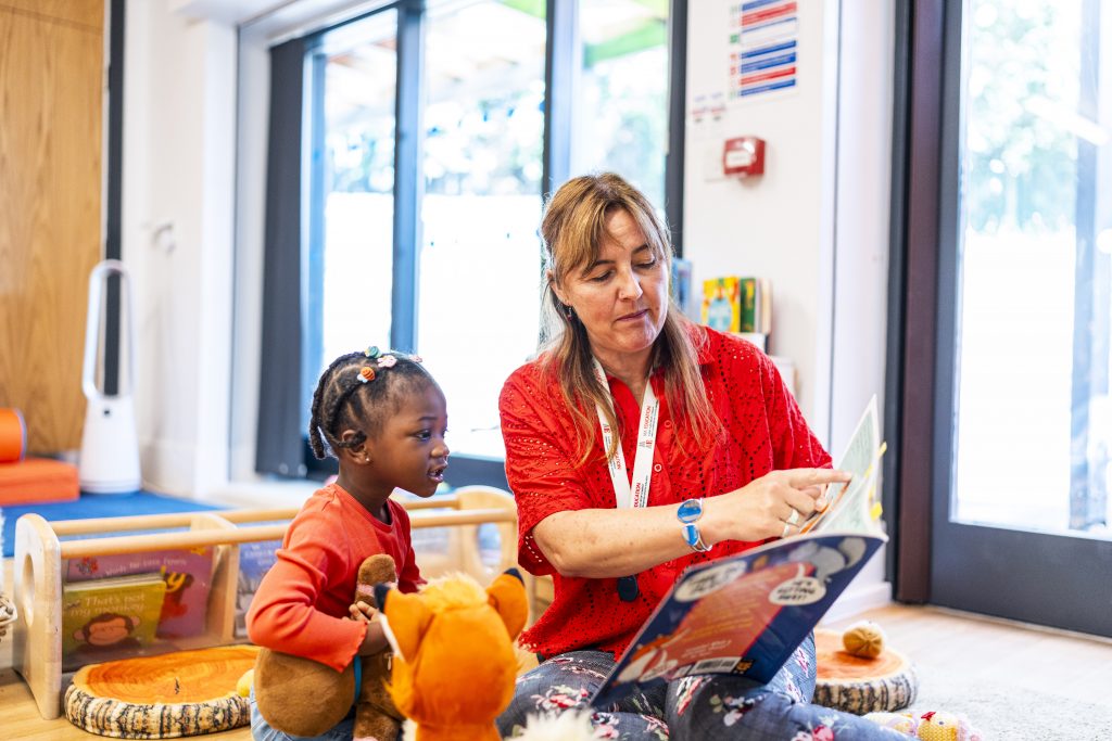 A teacher showing a child a page in a book, the girl is interested in what she is pointing at