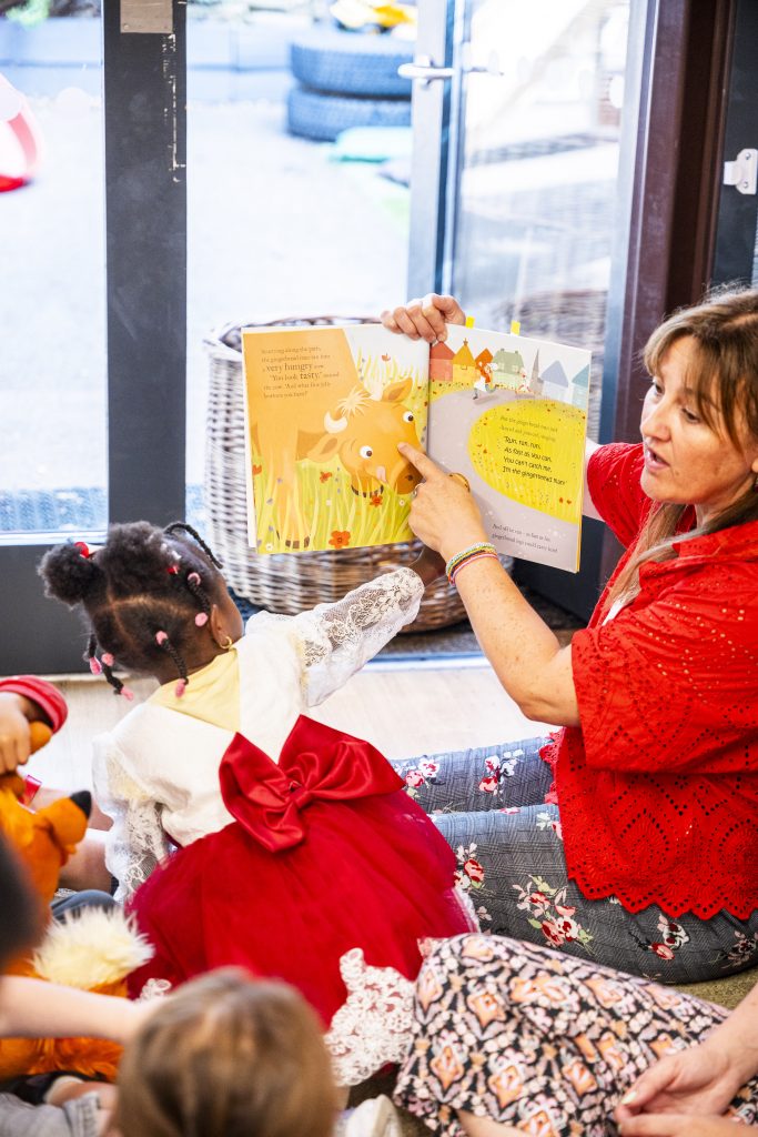 A teacher holding up a story book to show the children a picture